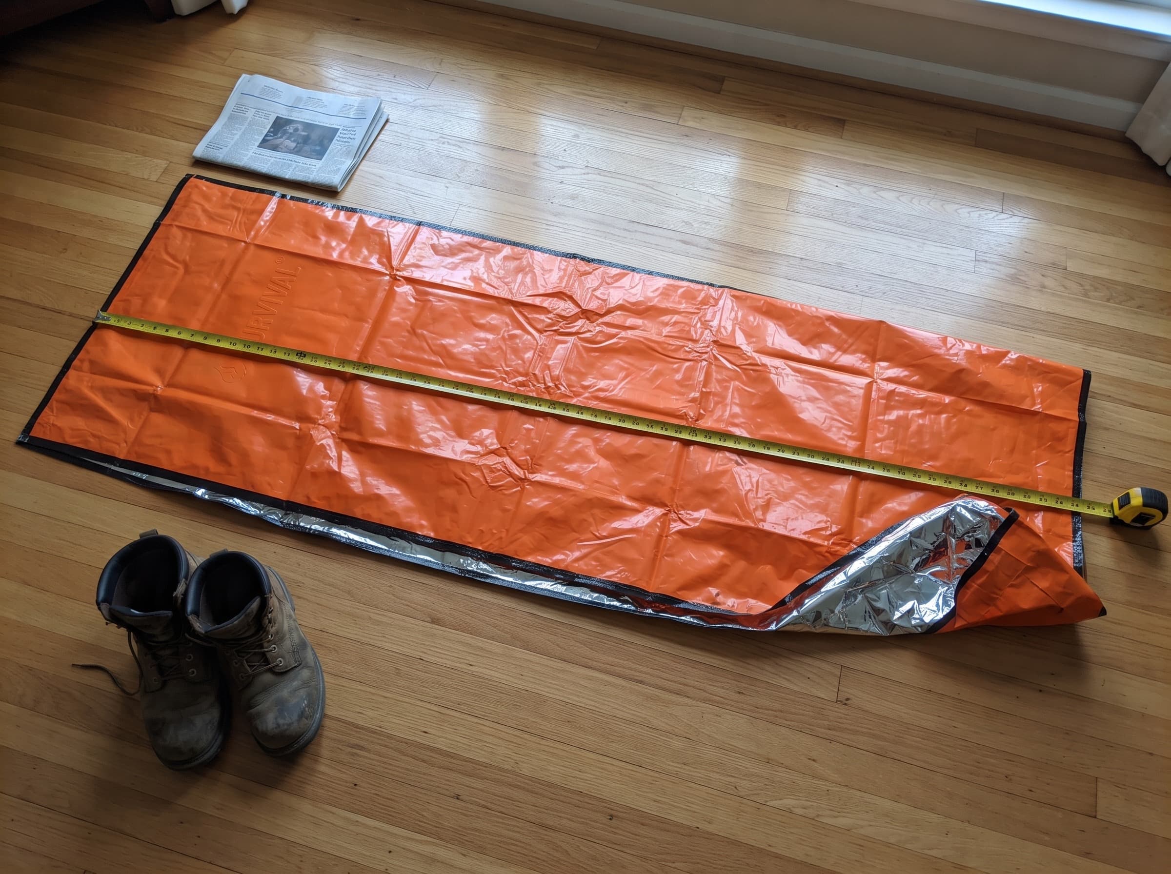 The emergency sleeping bag unfolded on a floor beside a tape measure showing its 7-foot length