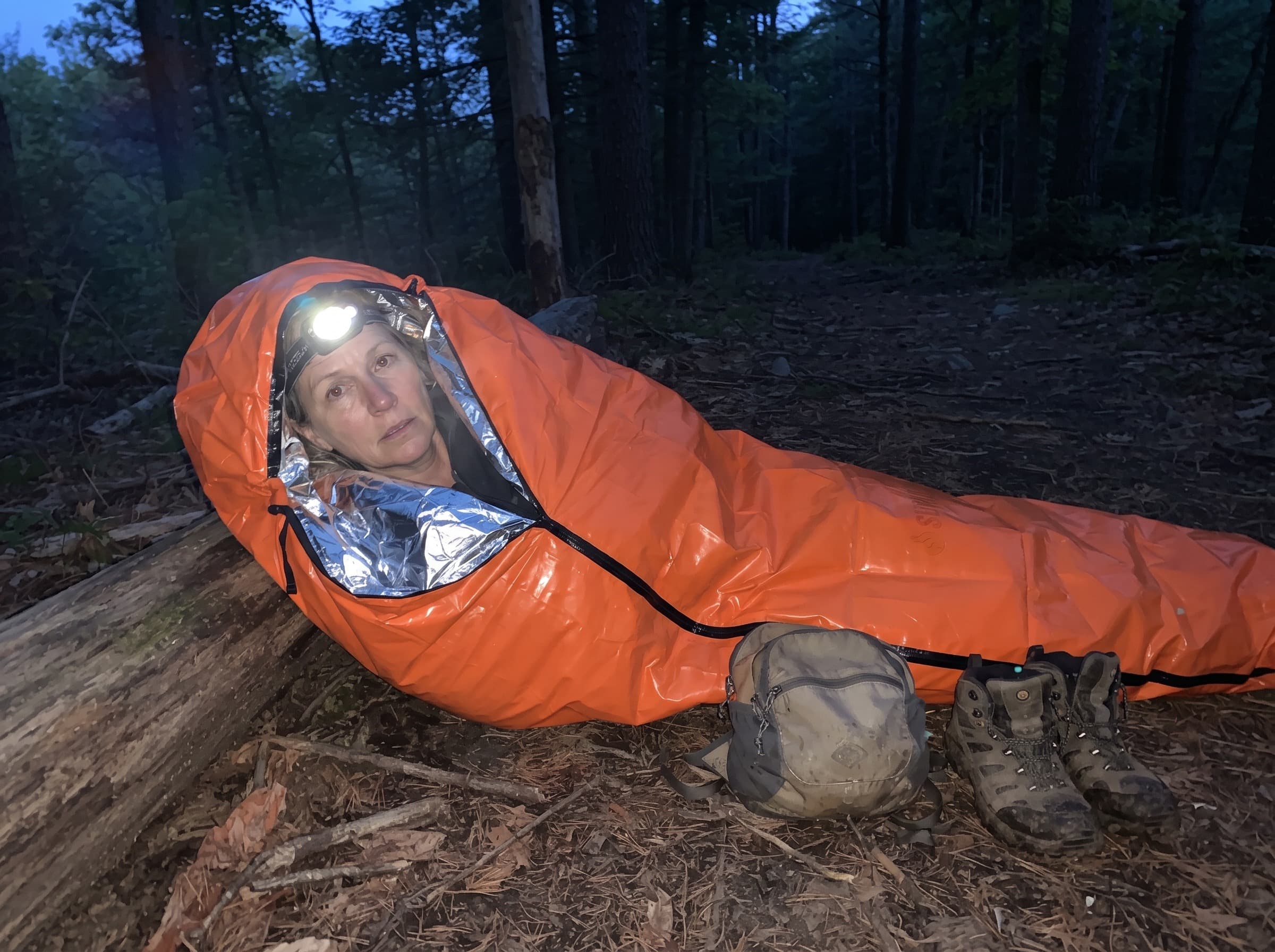 A woman lying inside the full-length emergency sleeping bag on a living room floor by lantern light during a power outage